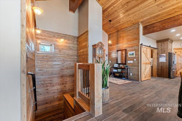 hall with dark wood-type flooring, a towering ceiling, a barn door, and wood walls