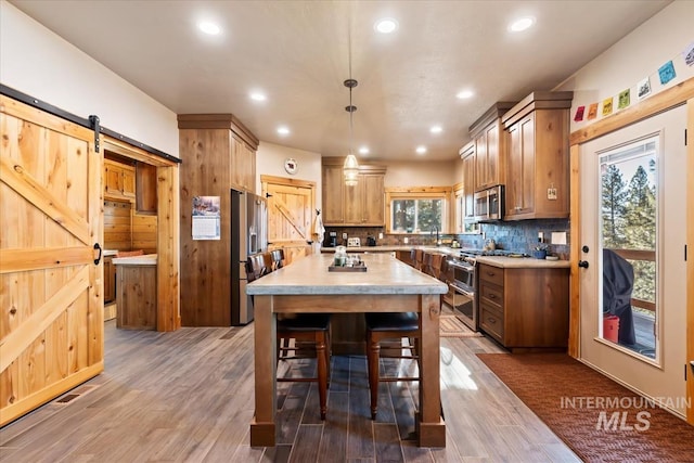 kitchen with premium appliances, dark hardwood / wood-style flooring, pendant lighting, a barn door, and decorative backsplash