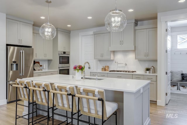 12039 N 19th Ave, Boise, ID 83714 - kitchen featuring stainless steel appliances, light wood-type flooring, light countertops, decorative backsplash, and a kitchen island with sink