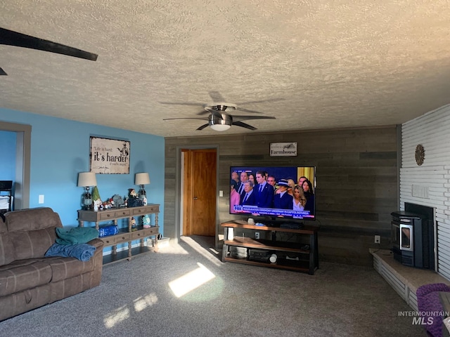 carpeted living room featuring ceiling fan, a wood stove, a textured ceiling, and wood walls