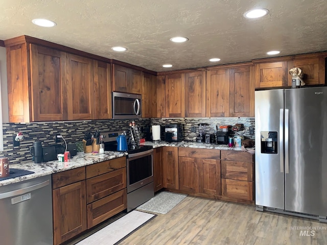 kitchen with light stone counters, backsplash, light hardwood / wood-style flooring, and appliances with stainless steel finishes