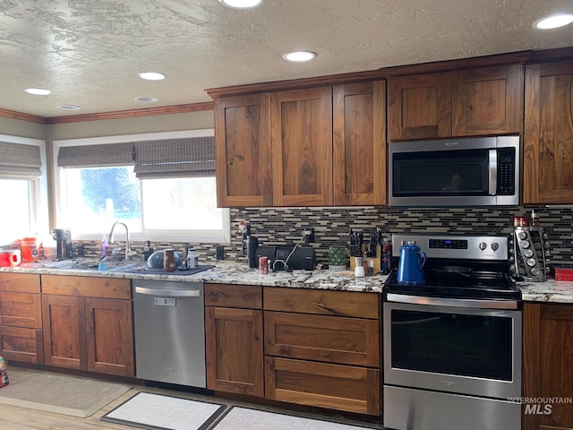 kitchen featuring light stone counters, appliances with stainless steel finishes, crown molding, and decorative backsplash