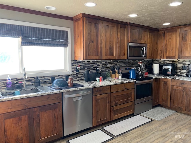 kitchen with sink, appliances with stainless steel finishes, light stone counters, tasteful backsplash, and light wood-type flooring