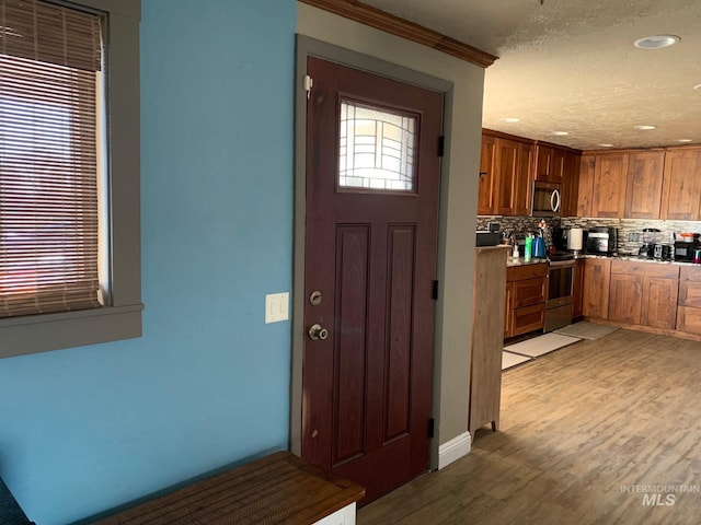 kitchen featuring backsplash, ornamental molding, stainless steel appliances, and light wood-type flooring