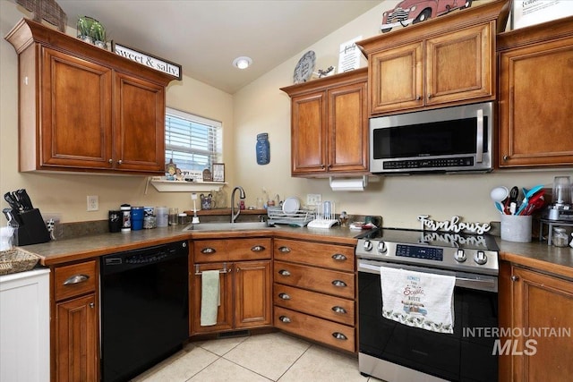 kitchen featuring lofted ceiling, light tile patterned floors, stainless steel appliances, a sink, and brown cabinets