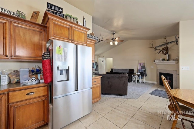 kitchen with light tile patterned floors, stainless steel fridge, brown cabinets, and a glass covered fireplace