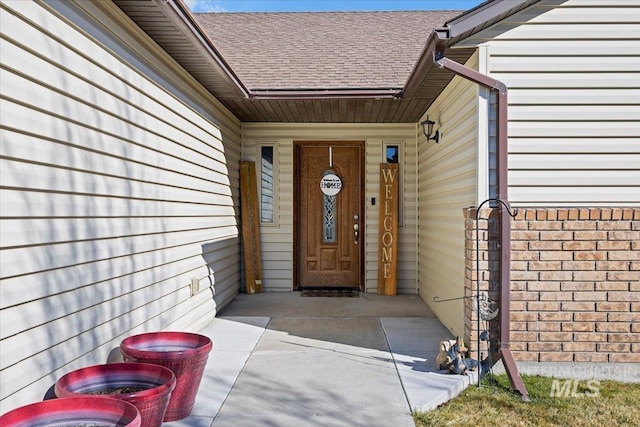 property entrance featuring roof with shingles and brick siding