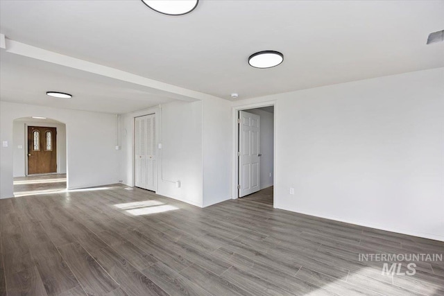 empty room with arched walkways, baseboards, and wood finished floors