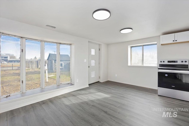 kitchen featuring baseboards, wood finished floors, stainless steel electric stove, and white cabinets