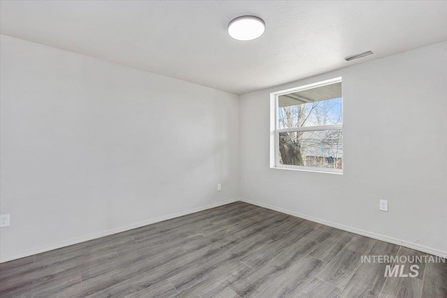 spare room featuring baseboards, visible vents, and wood finished floors