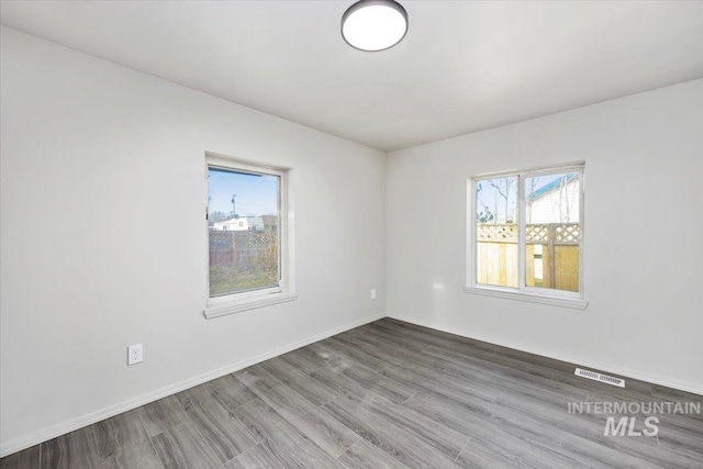 unfurnished room with baseboards, visible vents, and wood finished floors