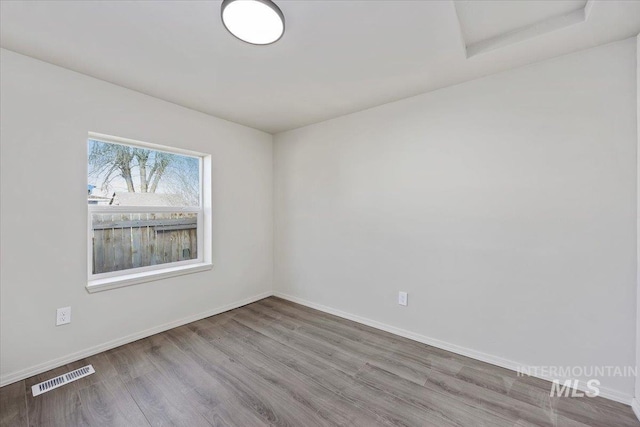 spare room featuring attic access, baseboards, visible vents, and wood finished floors