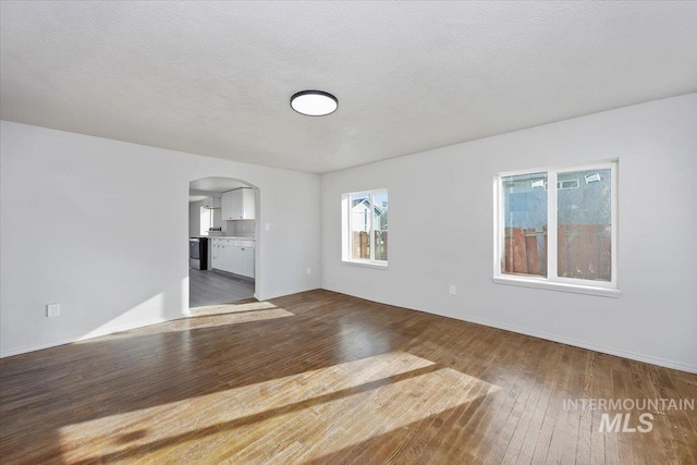spare room with arched walkways, a textured ceiling, and wood-type flooring