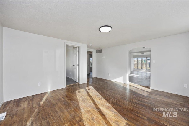 empty room featuring visible vents, arched walkways, a textured ceiling, and wood finished floors
