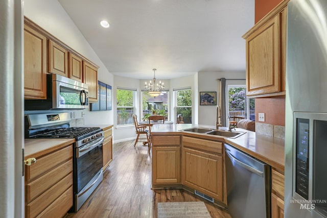 kitchen featuring stainless steel appliances, a sink, a peninsula, a chandelier, and dark wood finished floors