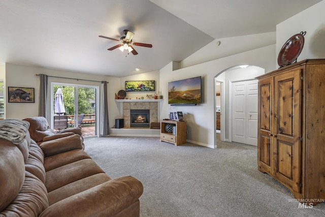living room with ceiling fan, arched walkways, carpet, vaulted ceiling, and a tile fireplace