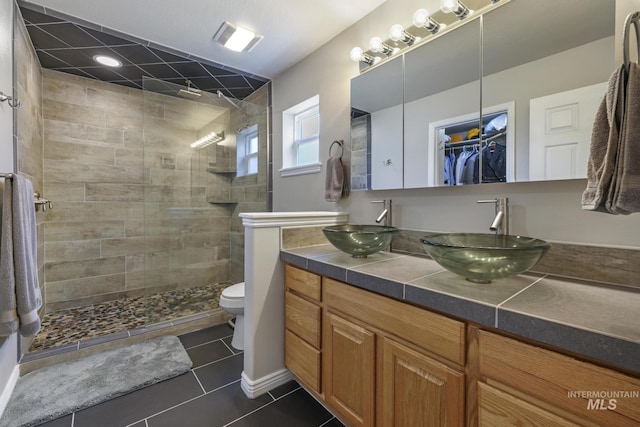 full bathroom featuring a tile shower, tile patterned flooring, toilet, and double vanity