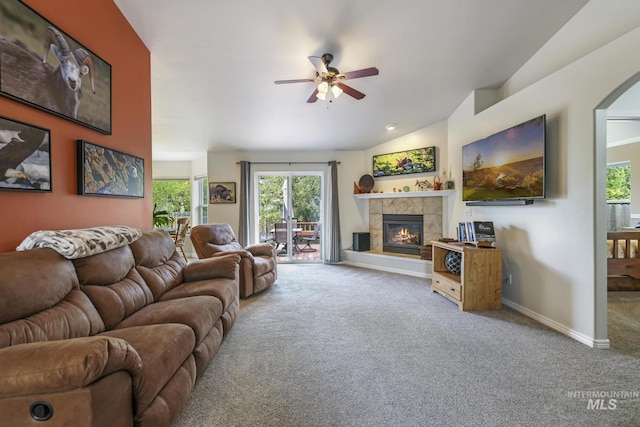 carpeted living room featuring a ceiling fan, a tiled fireplace, baseboards, and arched walkways