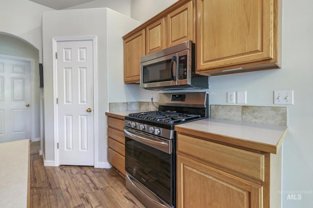 kitchen featuring stainless steel appliances, light countertops, light wood finished floors, arched walkways, and baseboards