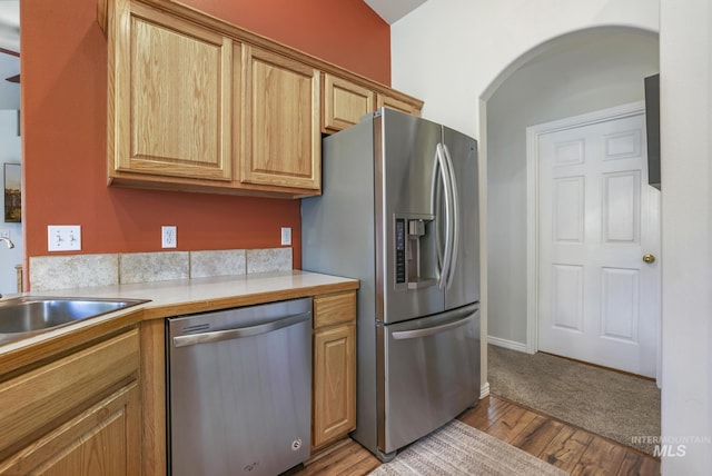 kitchen with appliances with stainless steel finishes, light countertops, light wood finished floors, and arched walkways