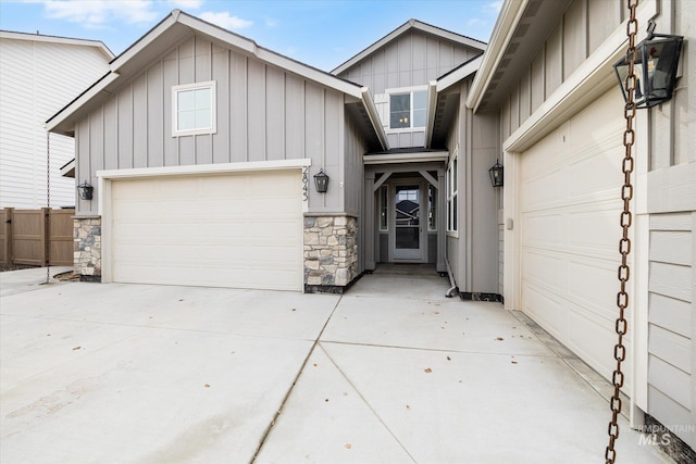 view of front of house with concrete driveway, stone siding, an attached garage, fence, and board and batten siding