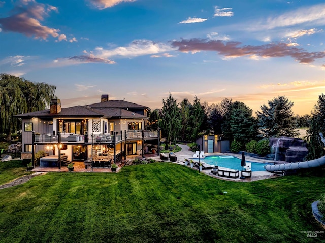 back house at dusk with a yard, a patio area, a balcony, and a storage unit