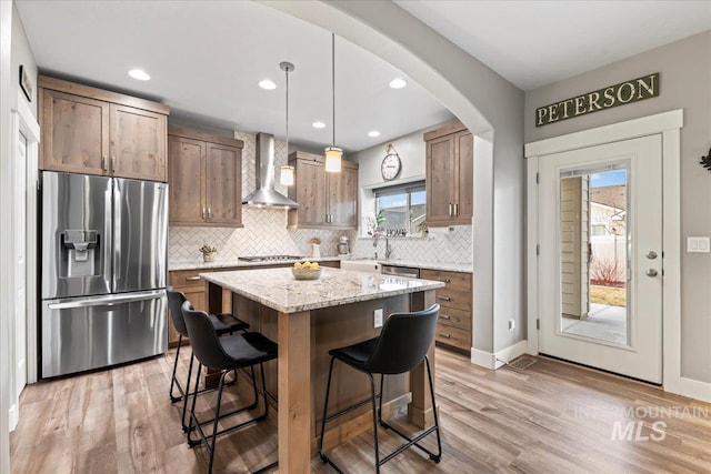 kitchen featuring backsplash, wall chimney range hood, a breakfast bar, light wood-style floors, and stainless steel appliances