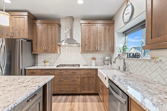 kitchen with light stone counters, appliances with stainless steel finishes, wall chimney exhaust hood, and a sink