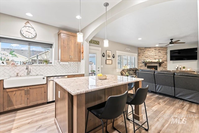 kitchen with light wood-style flooring, a fireplace, a sink, decorative backsplash, and dishwasher