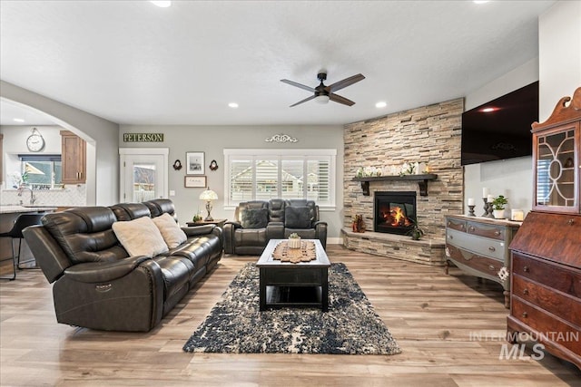 living area with a ceiling fan, light wood-style flooring, recessed lighting, a fireplace, and arched walkways