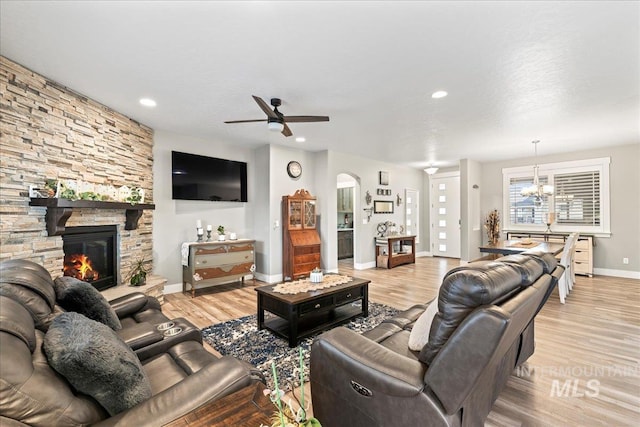 living area with light wood finished floors, baseboards, a stone fireplace, ceiling fan with notable chandelier, and recessed lighting