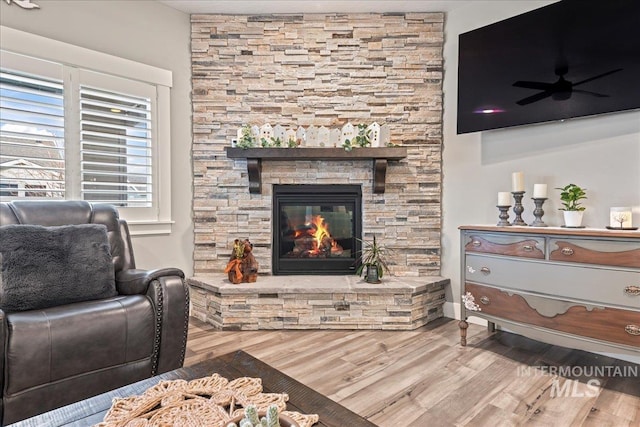 living area with a stone fireplace, wood finished floors, and ceiling fan