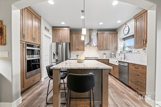 kitchen featuring stainless steel appliances, wall chimney exhaust hood, a center island, and light wood-style flooring