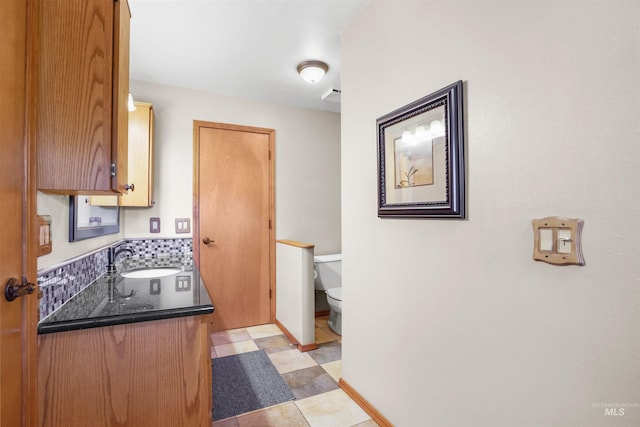 kitchen featuring a sink, baseboards, backsplash, brown cabinets, and dark countertops