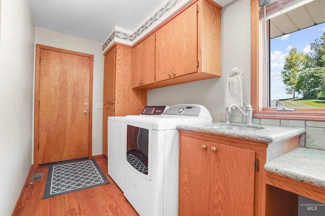 laundry area featuring light wood-style flooring, separate washer and dryer, a sink, visible vents, and cabinet space