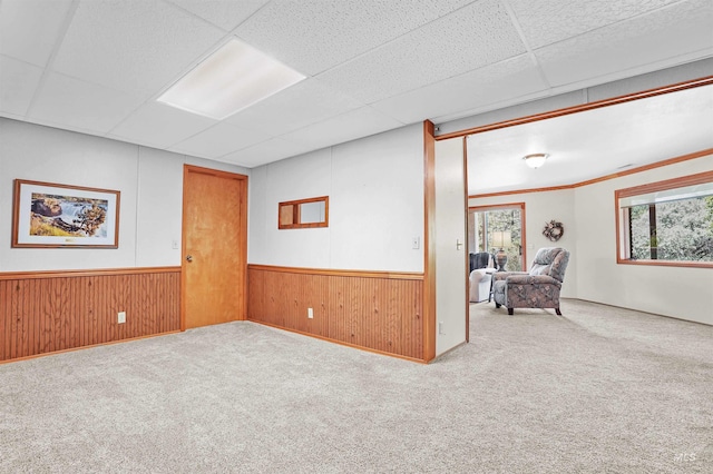 empty room featuring carpet floors, a drop ceiling, wainscoting, and wooden walls