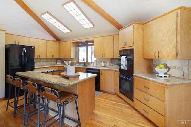 kitchen featuring light wood finished floors, lofted ceiling, a sink, black appliances, and a kitchen breakfast bar