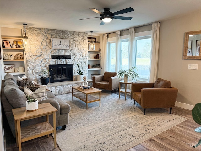 living area with a ceiling fan, wood finished floors, a fireplace, and baseboards