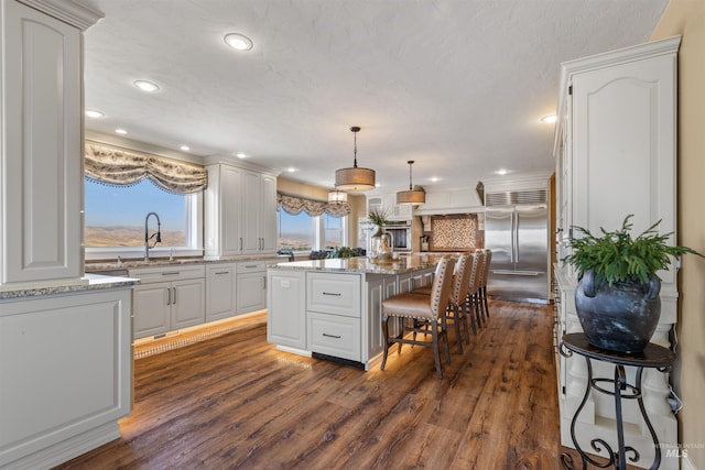 kitchen with pendant lighting, a center island, a breakfast bar, built in fridge, and sink