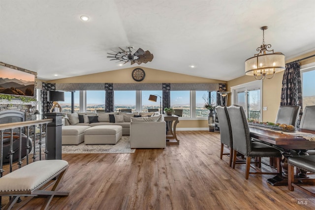 living room featuring hardwood / wood-style floors, ceiling fan with notable chandelier, lofted ceiling, and a stone fireplace