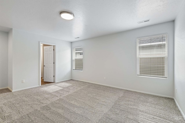 carpeted spare room featuring visible vents, baseboards, and a textured ceiling