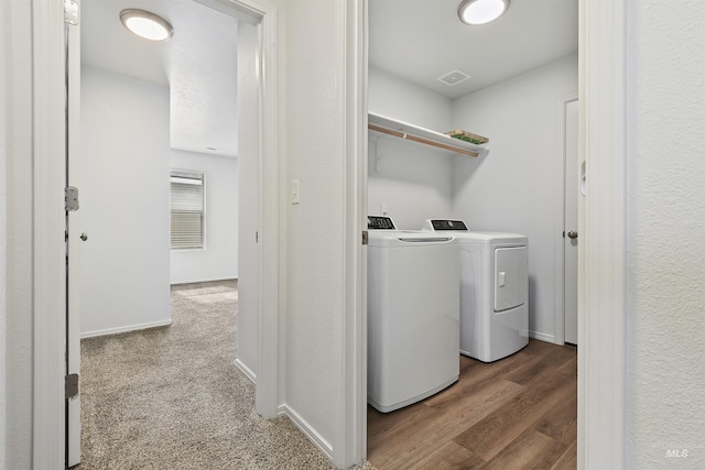 clothes washing area featuring washer and dryer, wood finished floors, carpet, baseboards, and laundry area