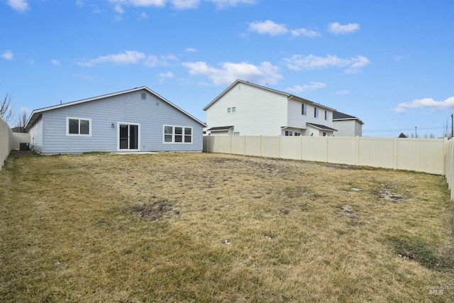 rear view of house with central AC unit, a lawn, and a fenced backyard