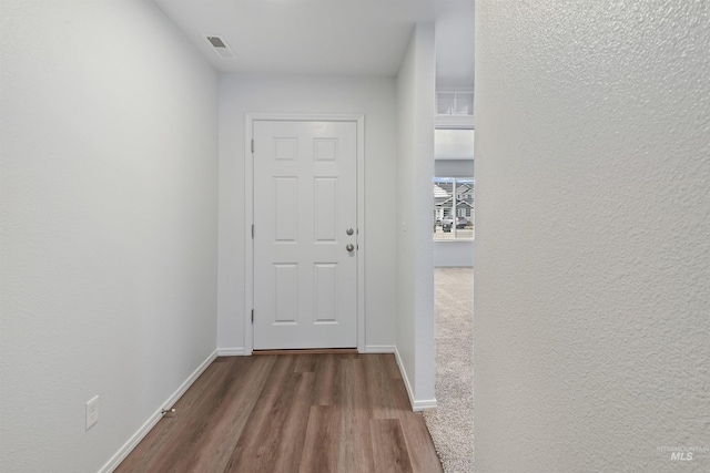 corridor with a textured wall, visible vents, baseboards, and wood finished floors