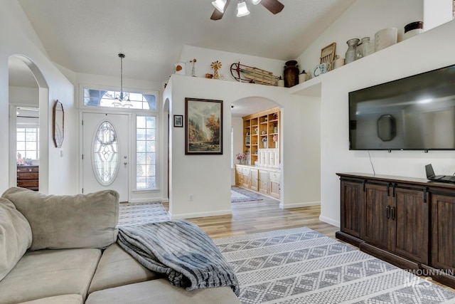 living area featuring a ceiling fan, light wood-style flooring, baseboards, and arched walkways