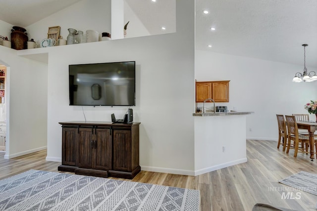 living area with baseboards, light wood finished floors, high vaulted ceiling, an inviting chandelier, and recessed lighting