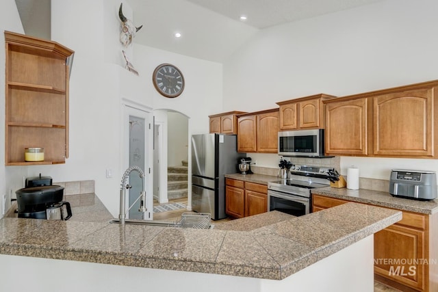 kitchen with tile counters, stainless steel appliances, arched walkways, high vaulted ceiling, and open shelves