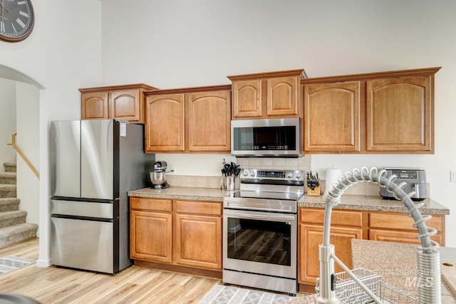 kitchen featuring tile countertops, arched walkways, light wood-style floors, appliances with stainless steel finishes, and a towering ceiling