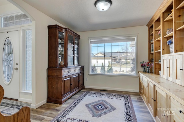 foyer with light wood-type flooring, arched walkways, a textured ceiling, and baseboards