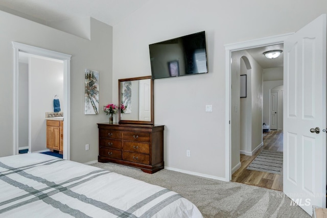 bedroom featuring baseboards, light carpet, arched walkways, and ensuite bath